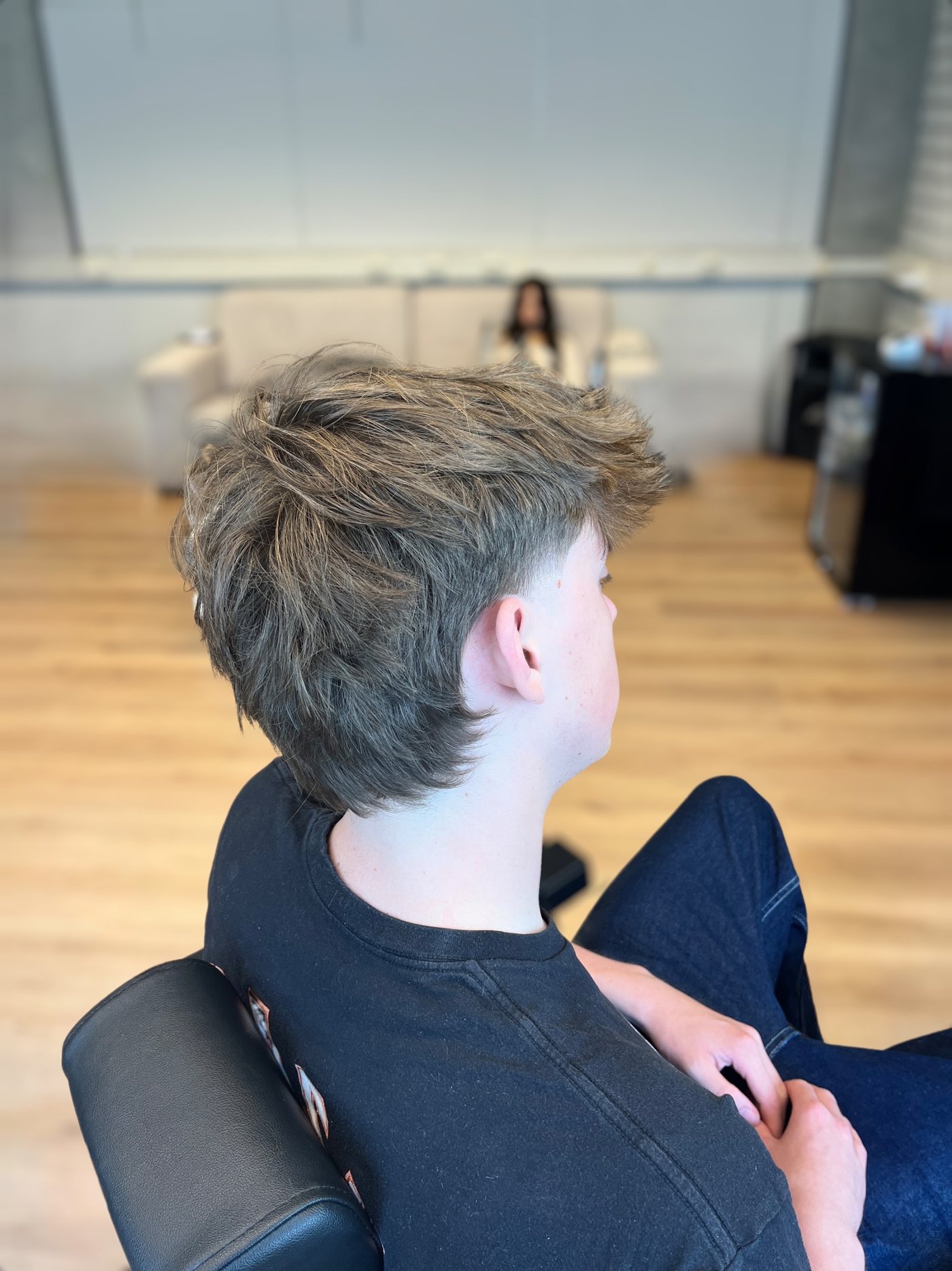Jonge klant met een getextureerd kapsel en fade, van achteren gezien in de zaak
