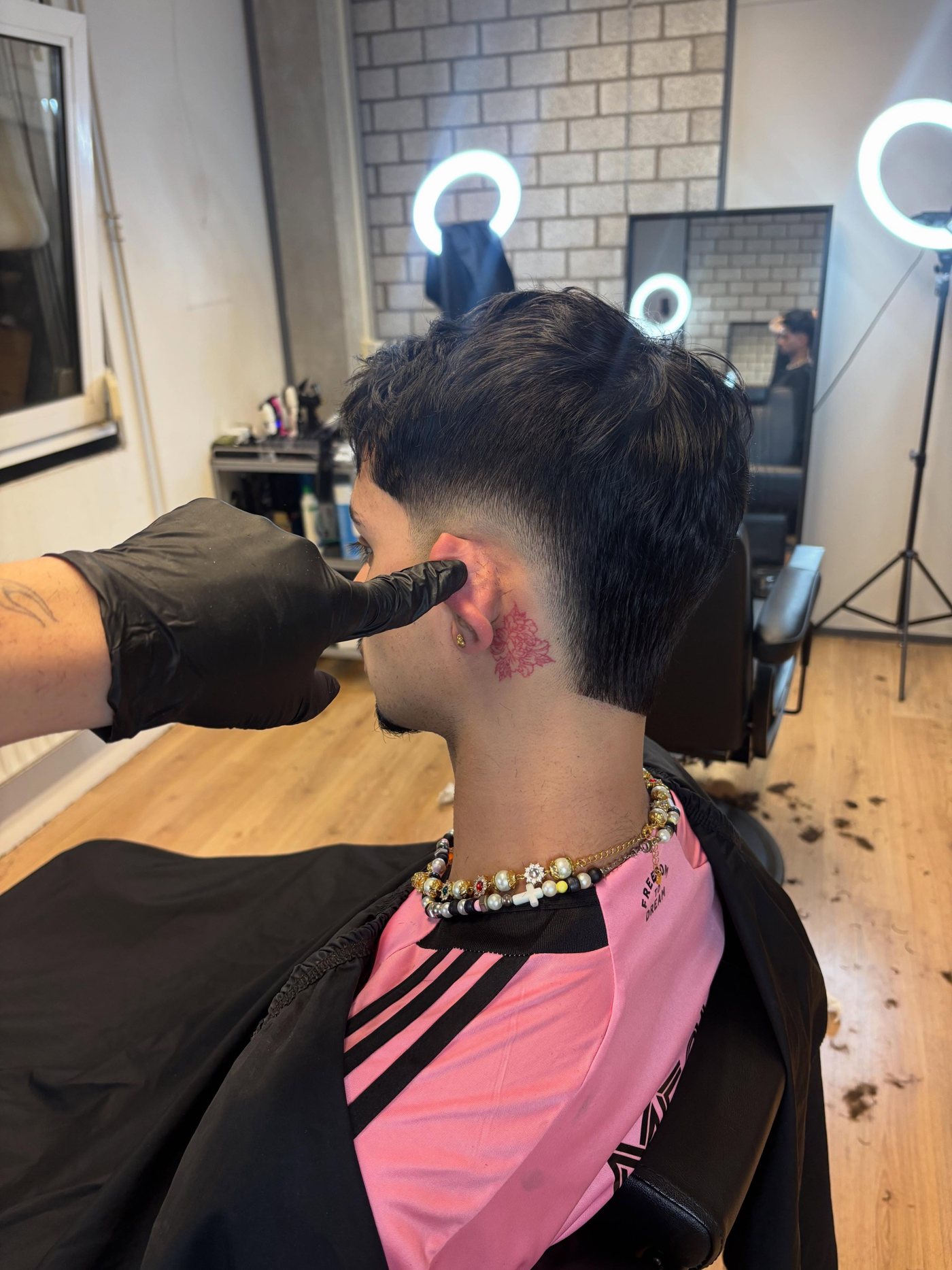 Barber aan het werk aan een mullet met taper, met de ringlampen van de zaak op de achtergrond